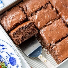 A closeup of a pan of chocolate cake with one slice on a spatula.