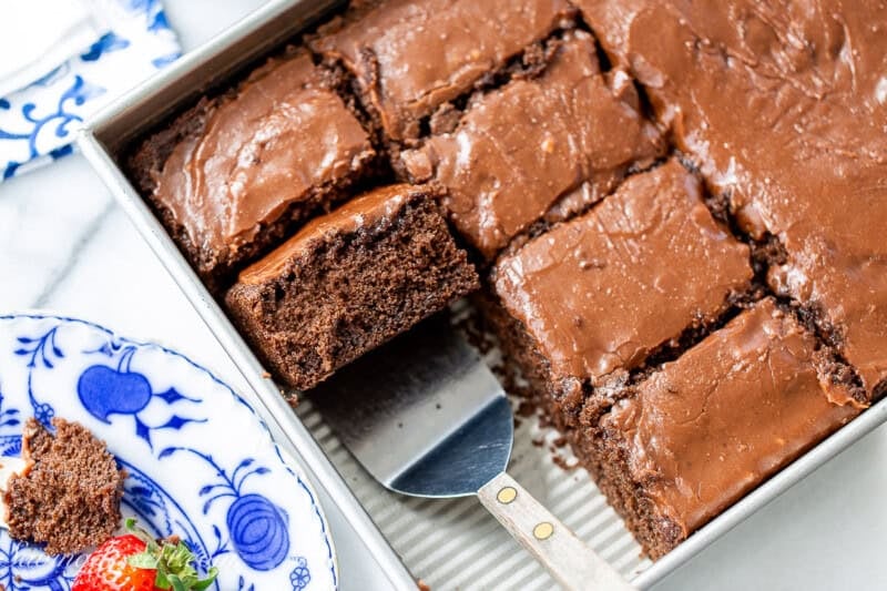 A closeup of a pan of chocolate cake with one slice on a spatula.