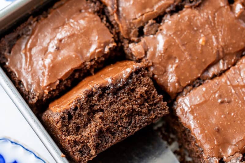 An overhead view of a pan of buttermilk chocolate cake with several slices removed and one on a spatula.