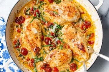 An overhead shot of a skillet of chicken breasts in a Parmesan cream sauce with wilted spinach and roasted cherry tomatoes.