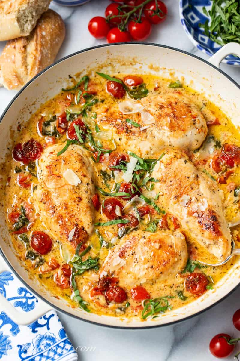An overhead skillet filled with chicken breasts, spinach and roasted tomatoes.