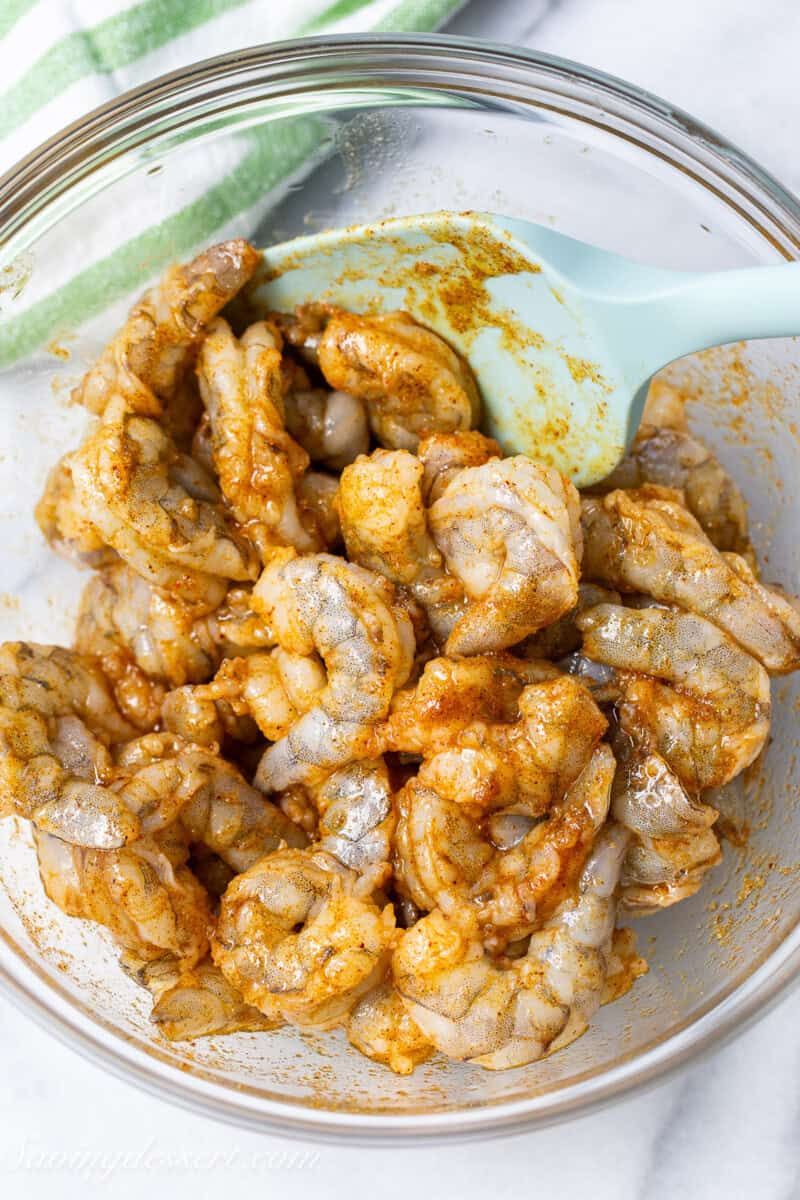 A bowl of raw shrimp being coated in a spice and oil mixture.