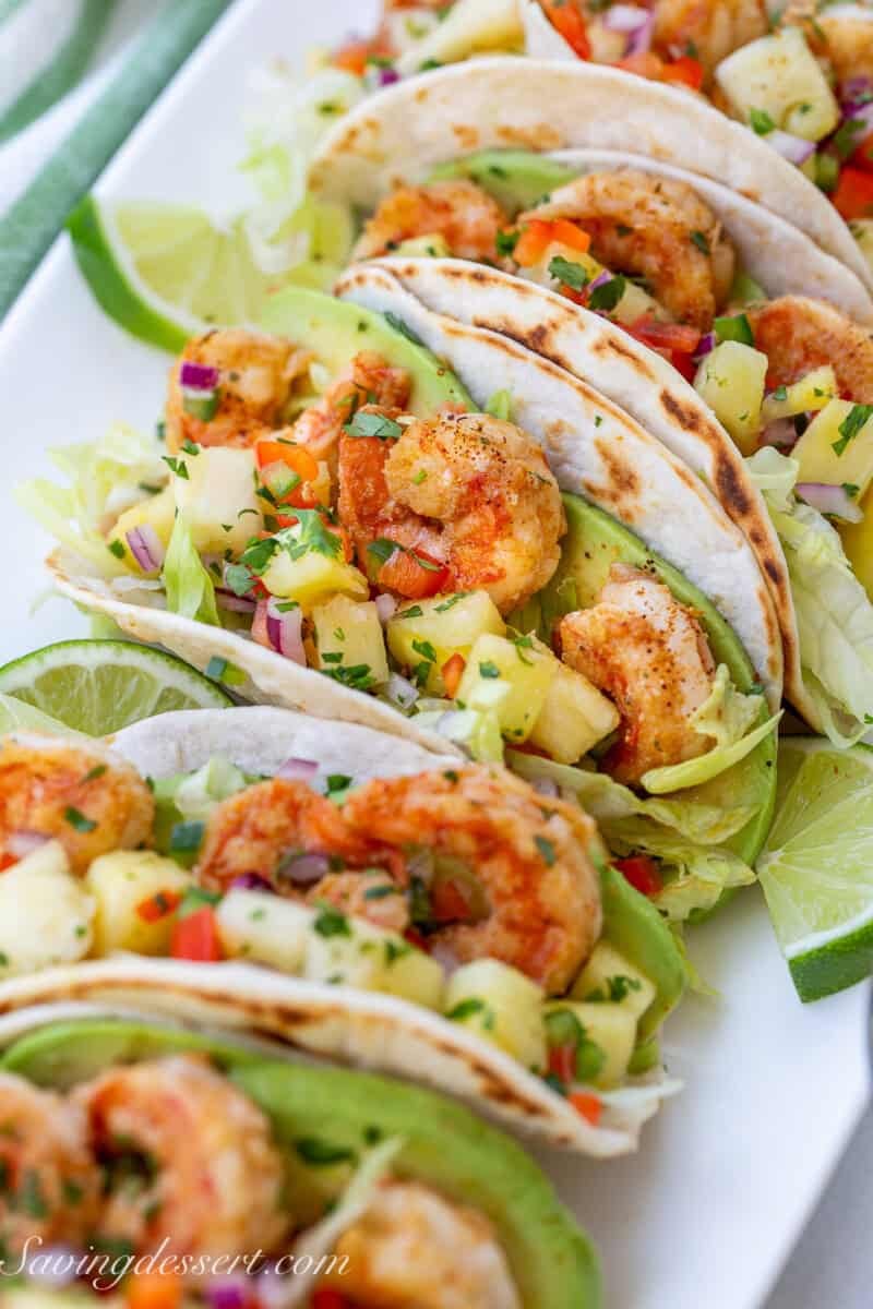 A row of shrimp tacos with salsa on a platter.