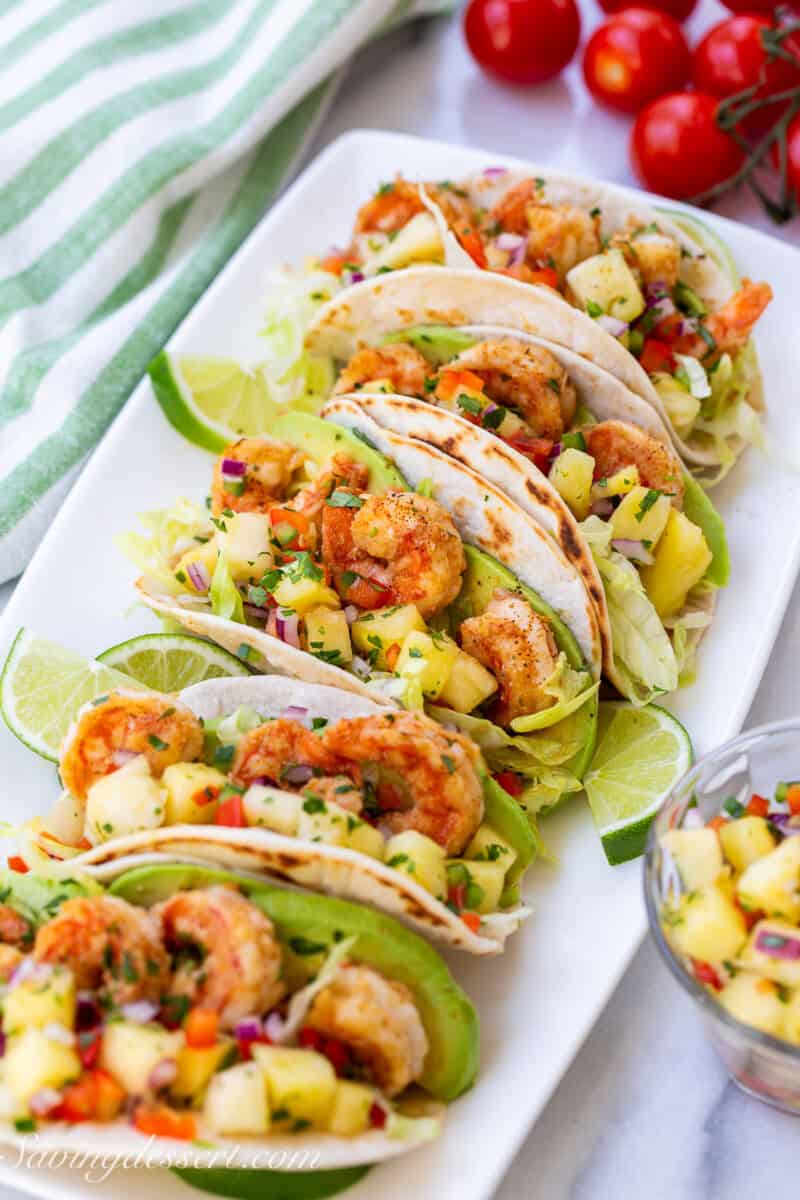 A platter of shrimp tacos with salsa on the side.