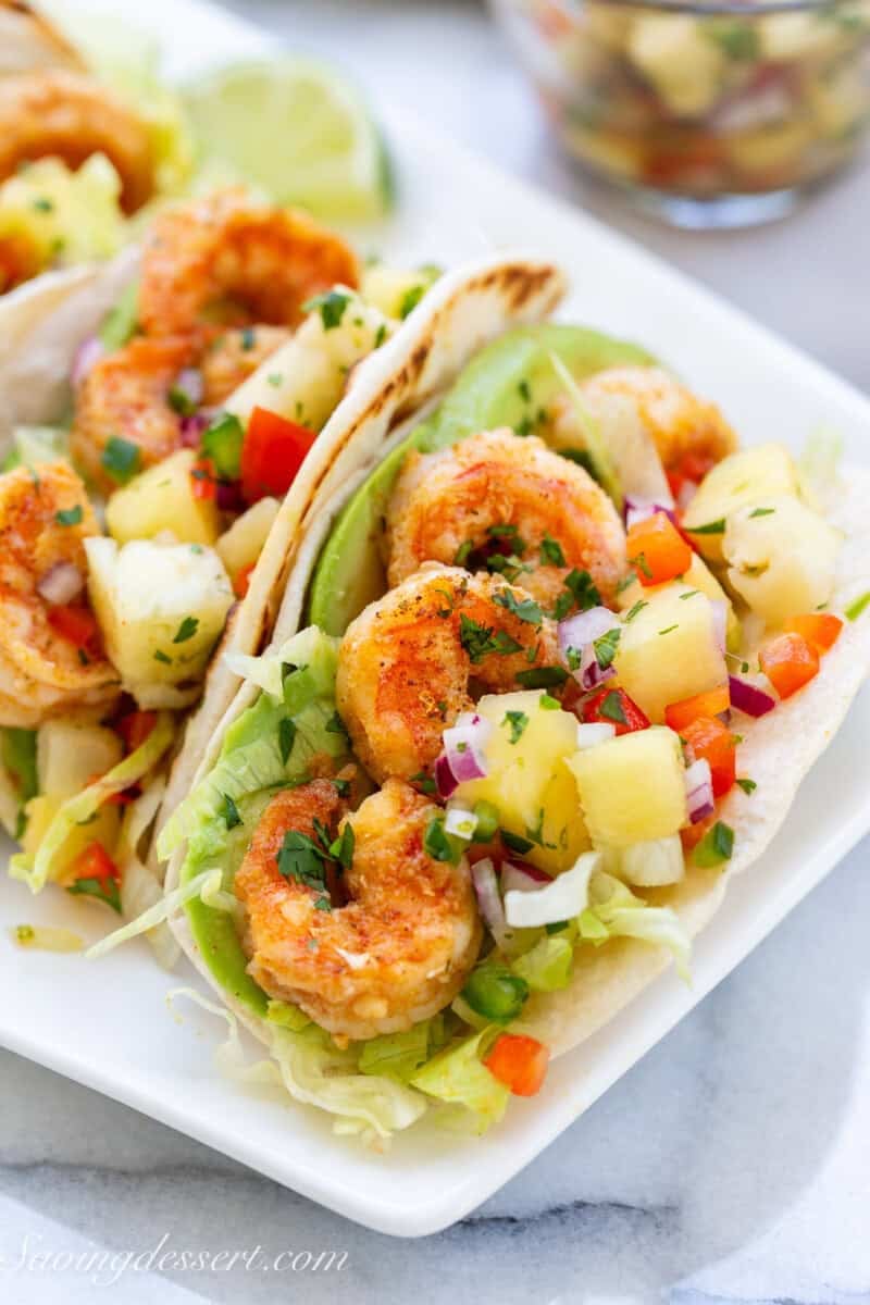 Shrimp tacos on a platter topped with salsa and avocado.