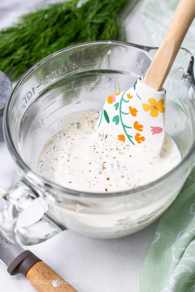 A mixing bowl with a spatula stirring homemade ranch dressing.