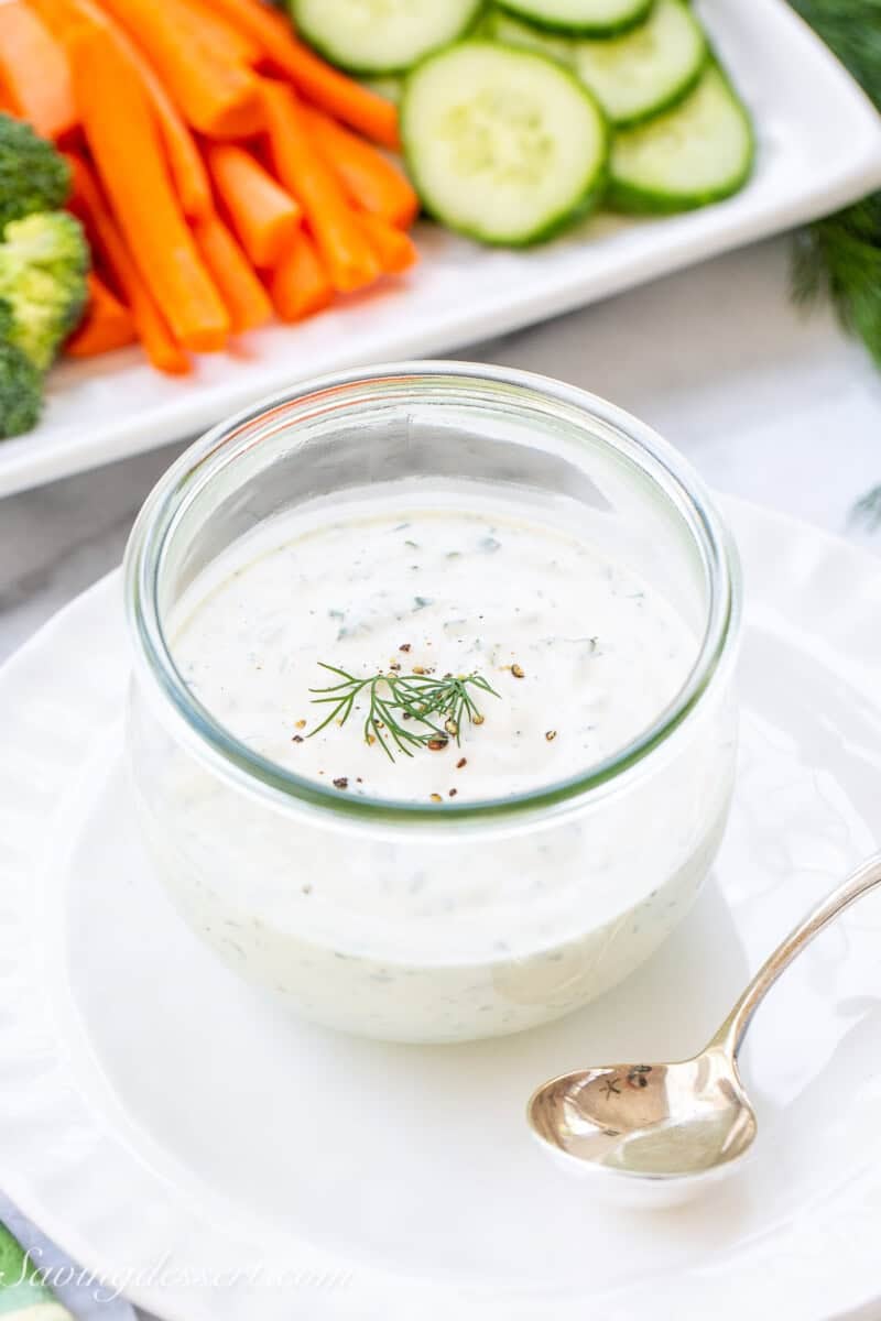 A jar filled with homemade ranch dressing topped with fresh dill and served with crudités.