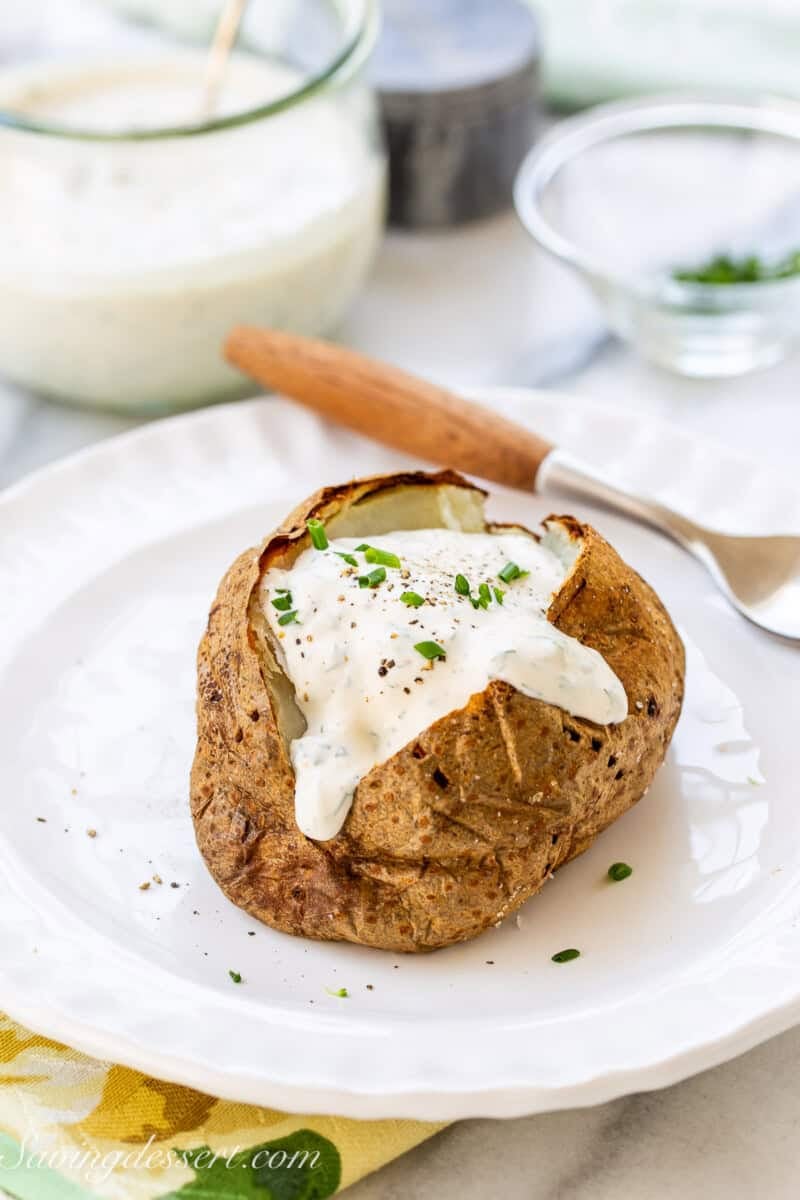 A baked potato on a plate with ranch dressing and chives on top.
