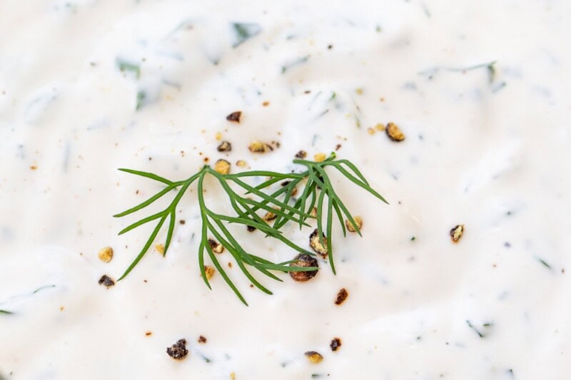 A closeup of a jar of ranch dressing with dill and black pepper on top.