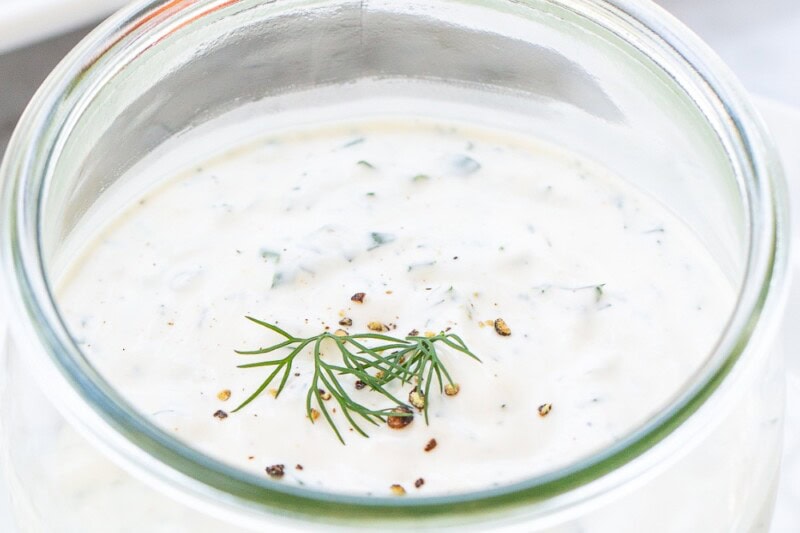 A jar filled with homemade ranch dressing topped with fresh dill.