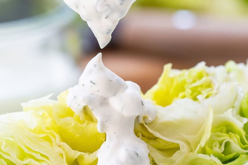 A lettuce wedge being drizzled with thick ranch dressing.