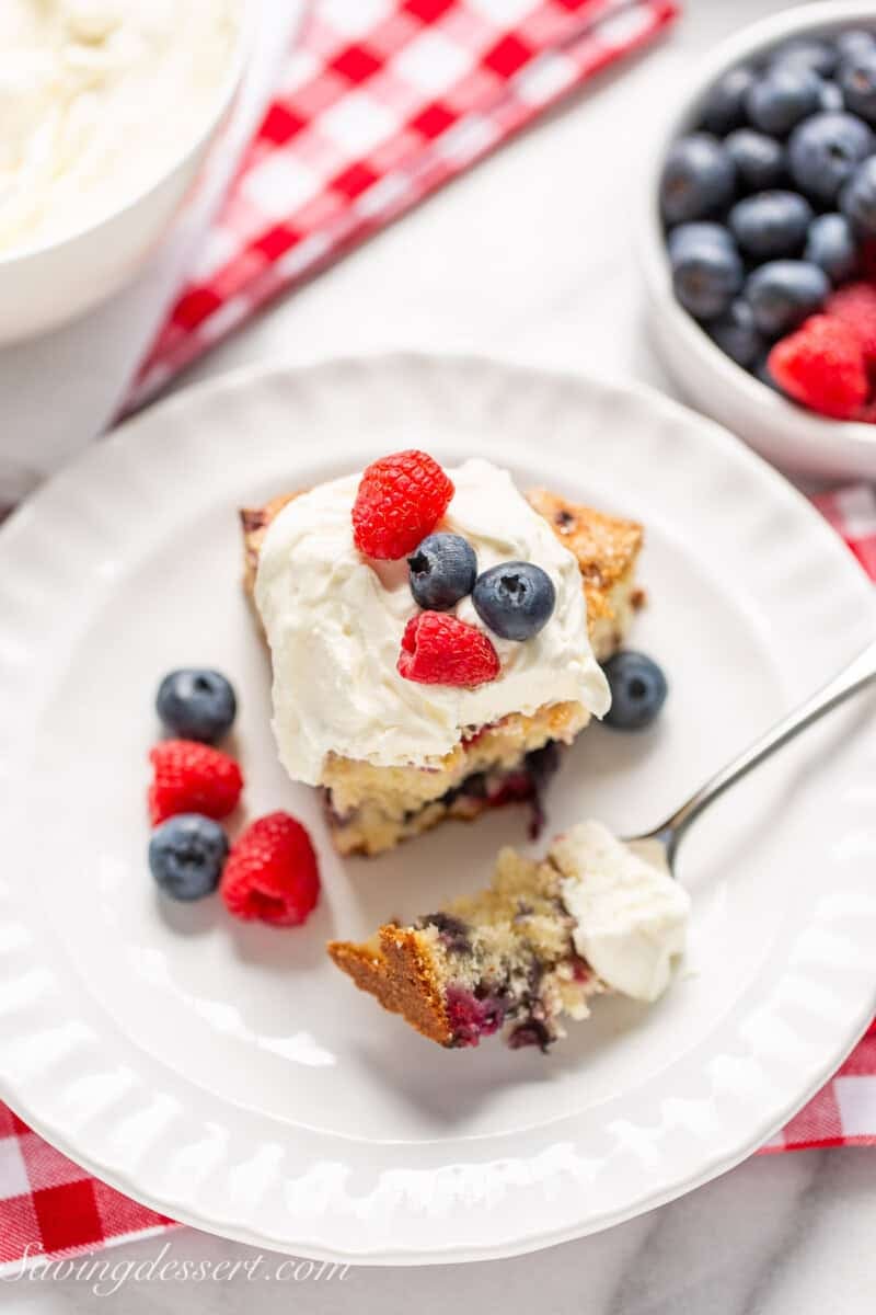 An overhead view of a partially eaten slice of red white and blue cake with whipped cream on top.