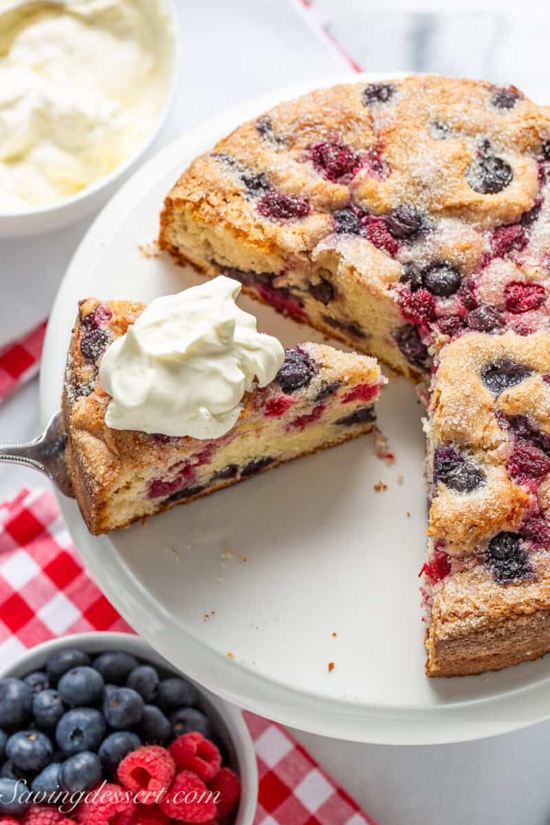 An overhead photo of a single layered red white and blue cake on a cake stand with one slice topped with whipped cream.