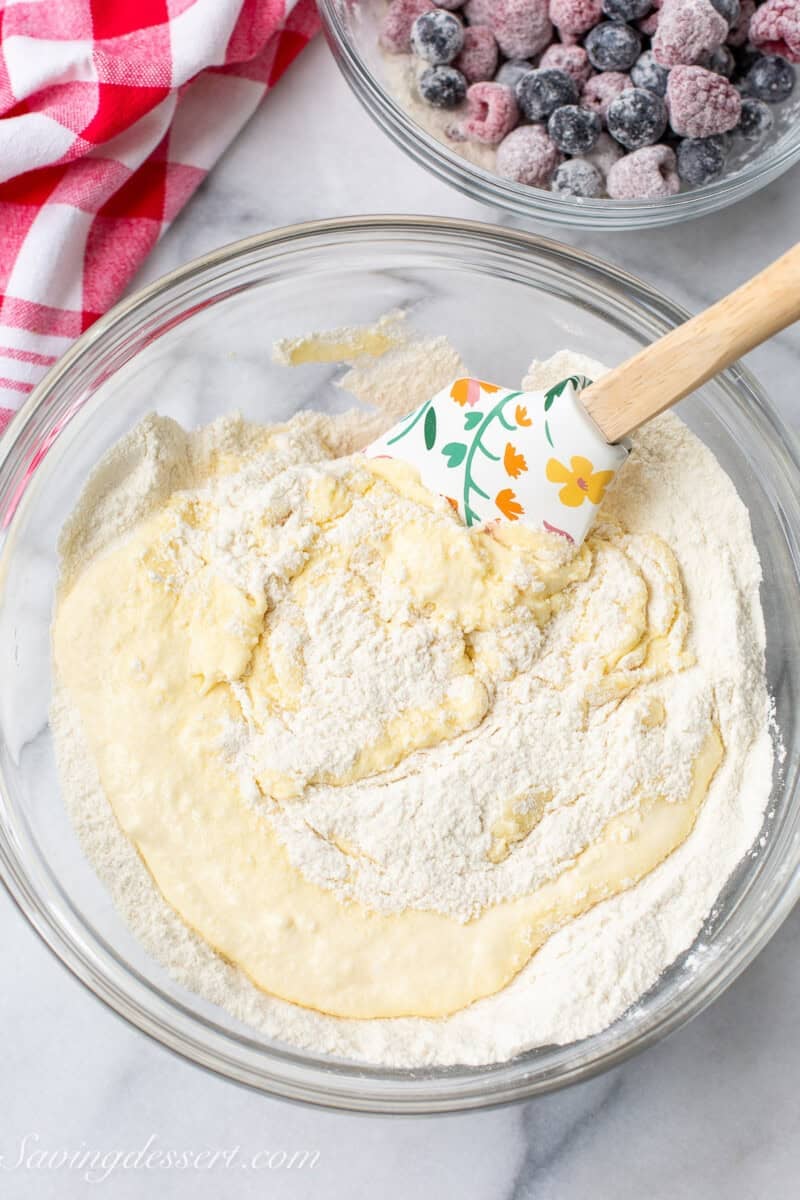 A bowl of cake batter with flour dusted berries in a bowl on the side.