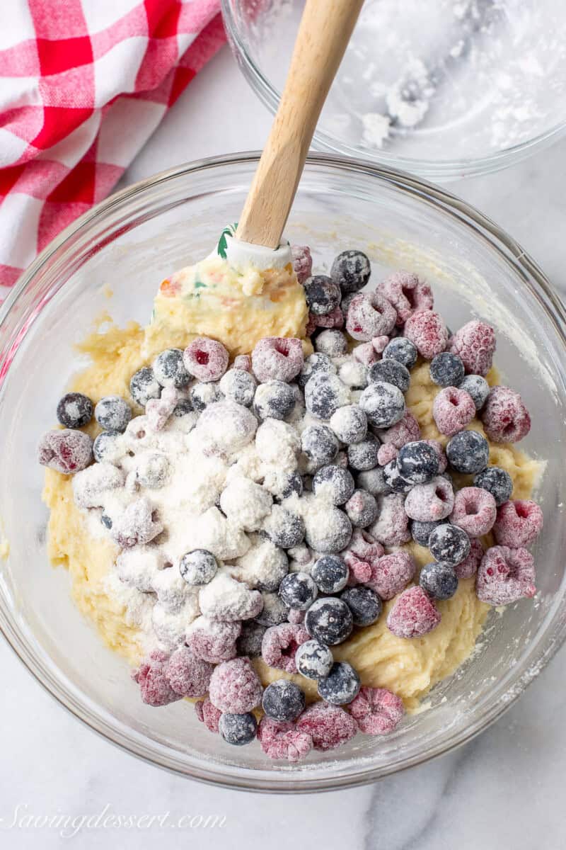 A bowl of cake batter with flour dusted berries being folded in.