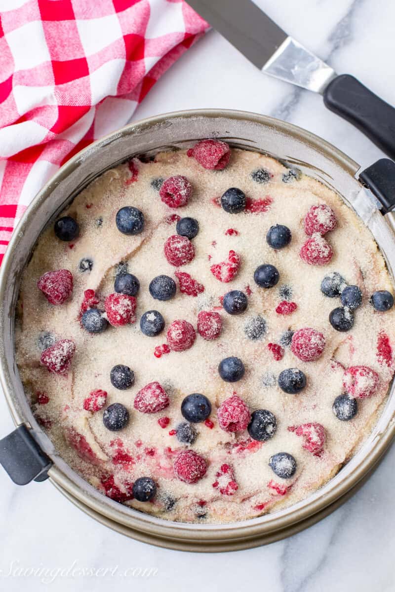 A spring form pan filled with cake batter topped with fresh raspberries and blueberries.
