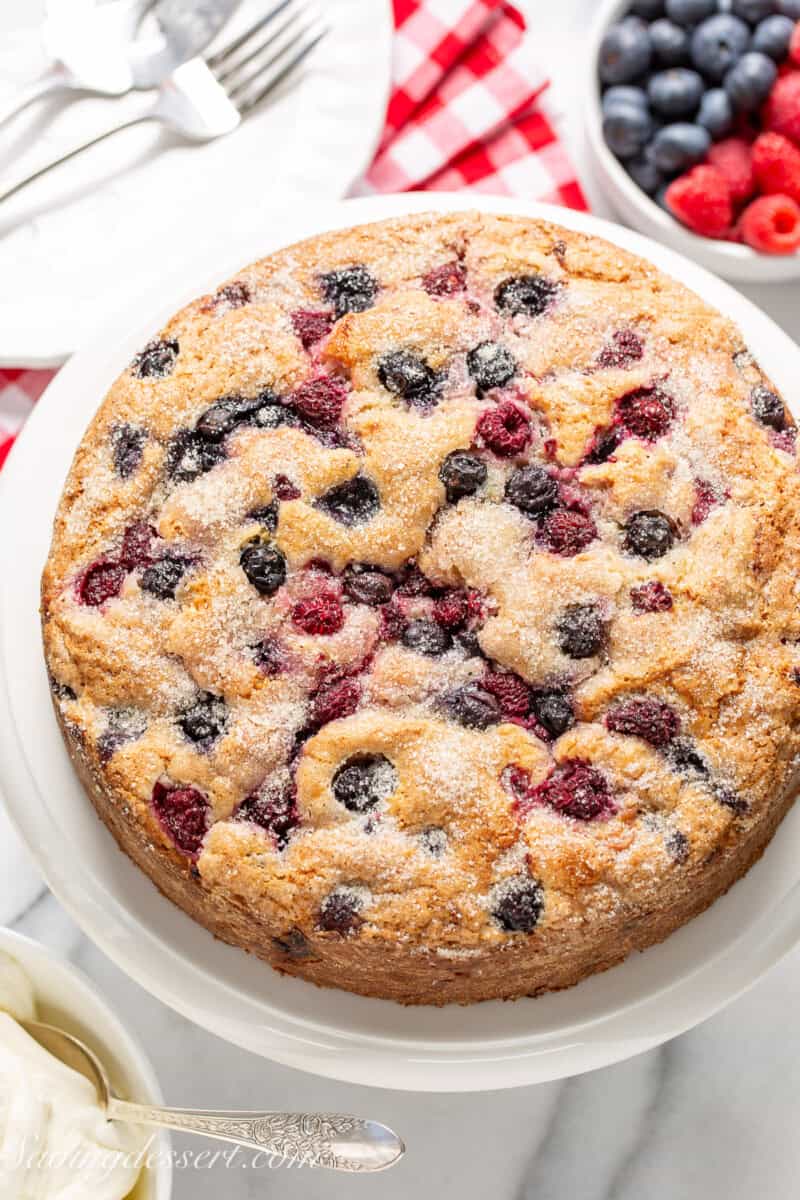 An overhead photo of a blueberry and raspberry cake on a cake stand.