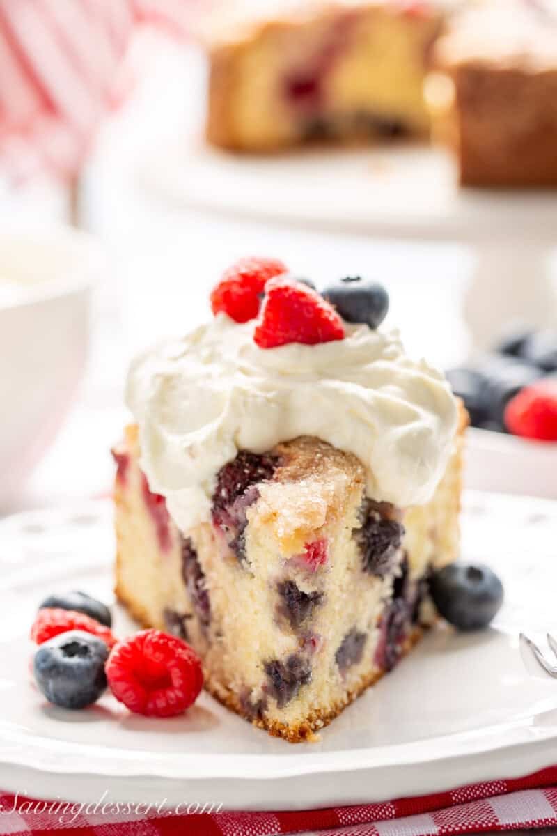 A closeup of a slice of berry filled cake with whipped cream on top.