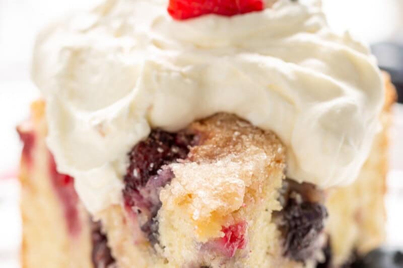 A closeup of a berry filled single layer cake topped with whipped cream and fresh raspberries and blueberries.