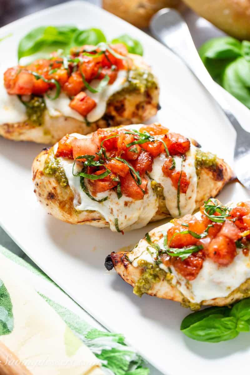 A platter with three cooked chicken breasts topped with melted mozzarella and a tomato bruschetta topping.