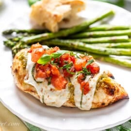 A closeup of a piece of chicken caprese on a plate with asparagus.