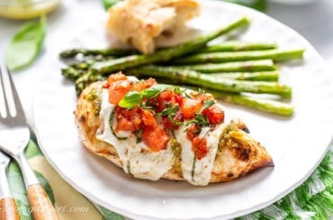 A closeup of a piece of chicken caprese on a plate with asparagus.