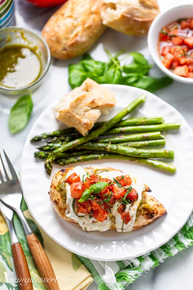 An overhead shot of a plate with chicken caprese, asparagus and a hunk of crusty bread.