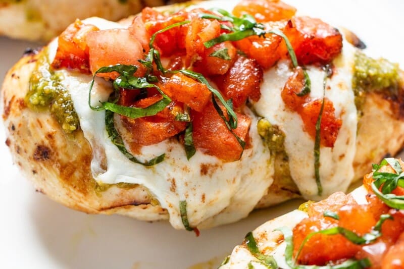 Mozzarella covered chicken breasts on a platter with bruschetta topping.