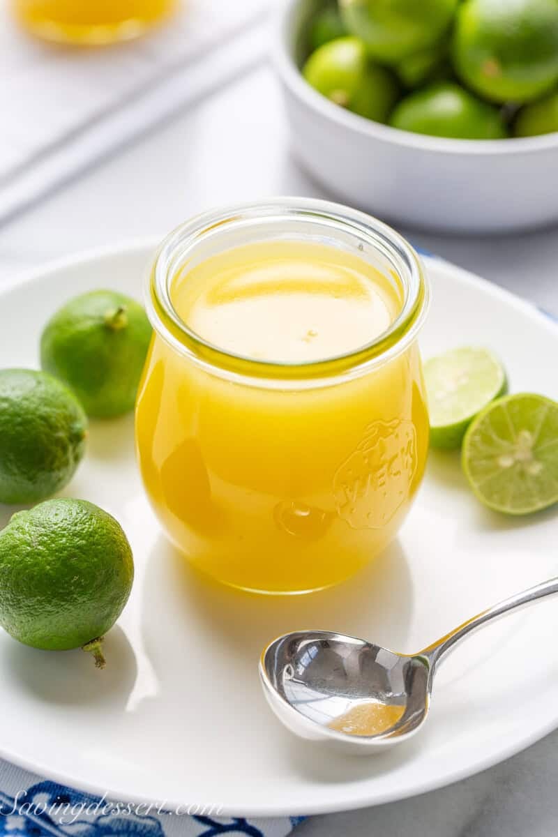 A jar filled with fresh key lime curd with a small ladle on a plate.
