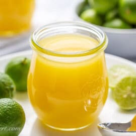 A side view of a jar of key lime curd on a plate.