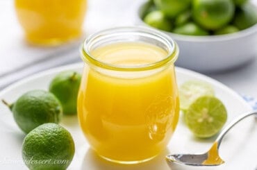 A side view of a jar of key lime curd on a plate.