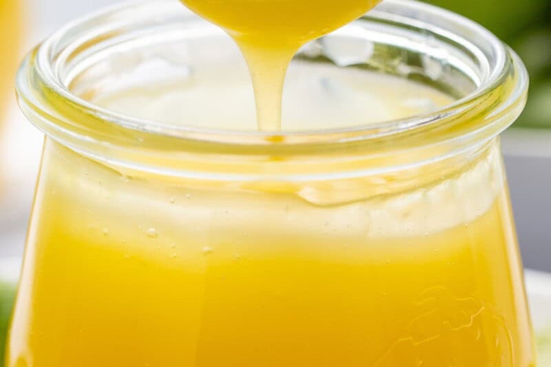 Key Lime Curd being drizzled into a jar from a small spoon.