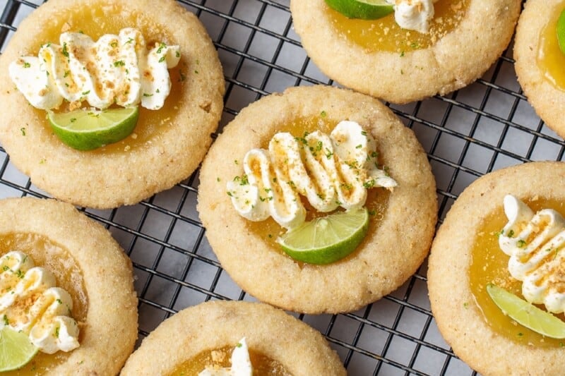 Key lime pie cookies decorated with swirls of whipped cream, key lime wedges and crushed graham crackers.