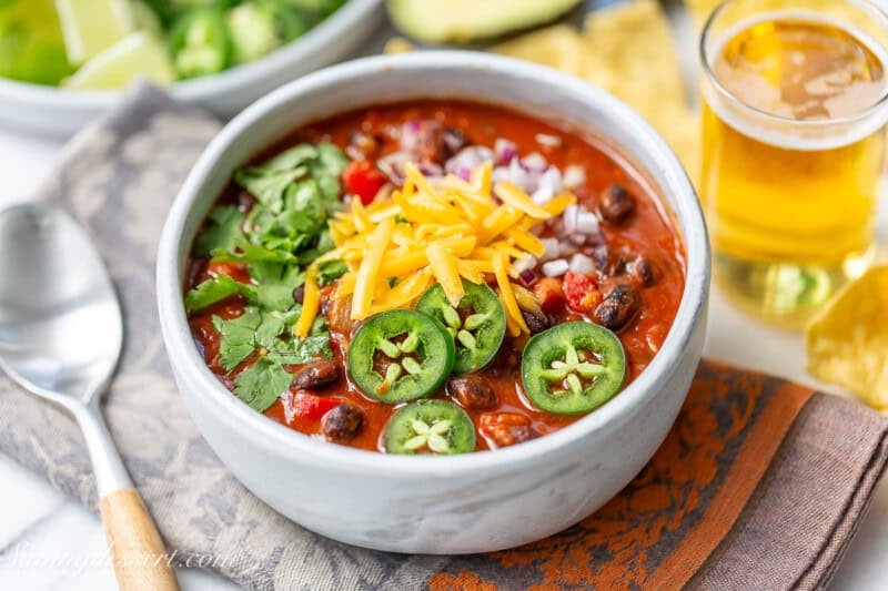 Black bean chili in a bowl topped with garnishes like shredded cheese, sliced jalapenos and cilnatro.
