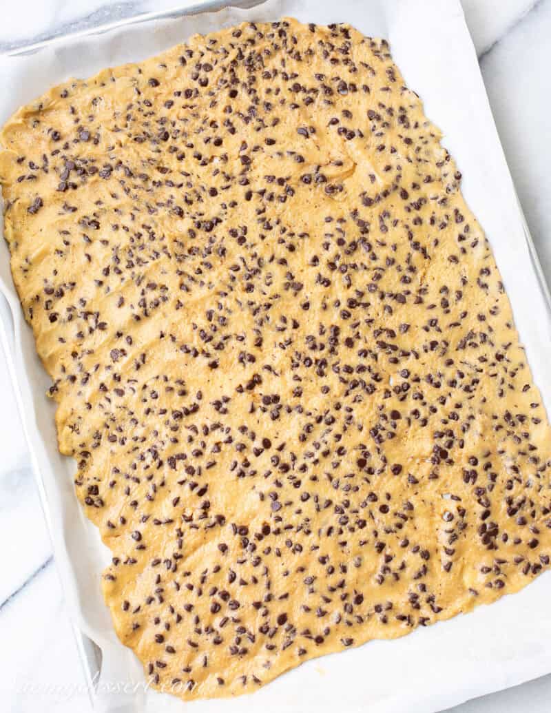 Chocolate chip cookie dough spread thin on a baking sheet.