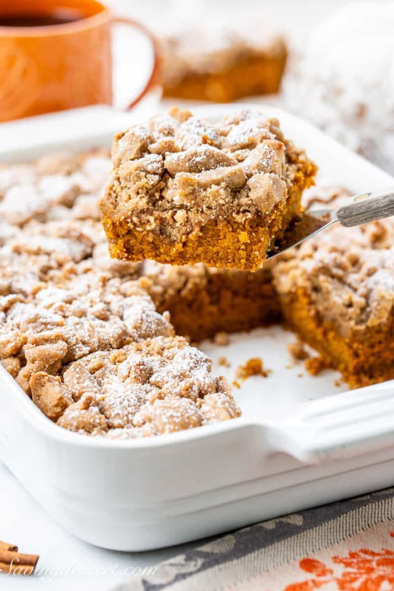 A pumpkin crumb cake in a baking pan with one piece being lifted out with a spatula.