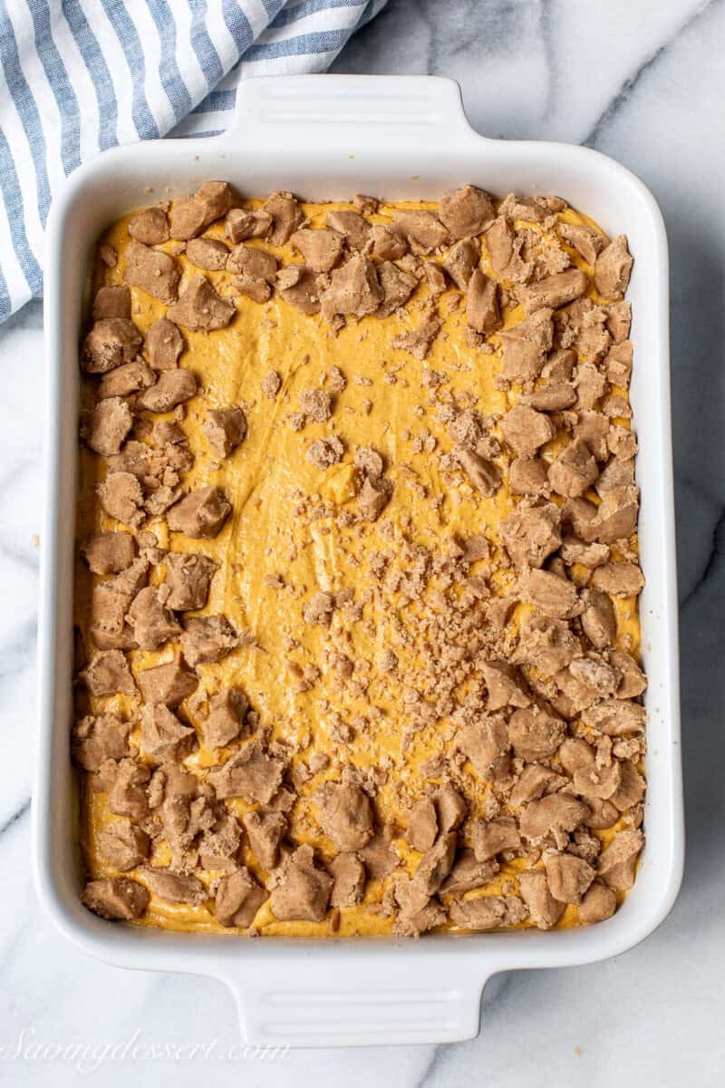 Pumpkin cake batter in a pan with crumbs being sprinkled on top.