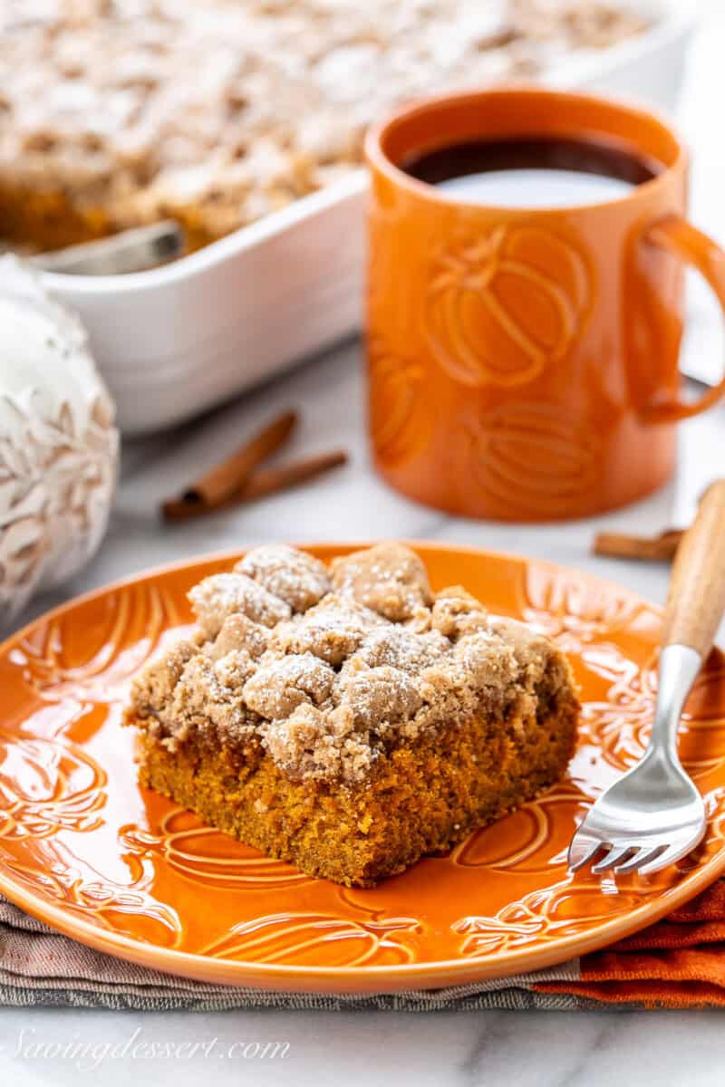 Pumpkin crumb cake on an orange plate with a fork and a cup of coffee.