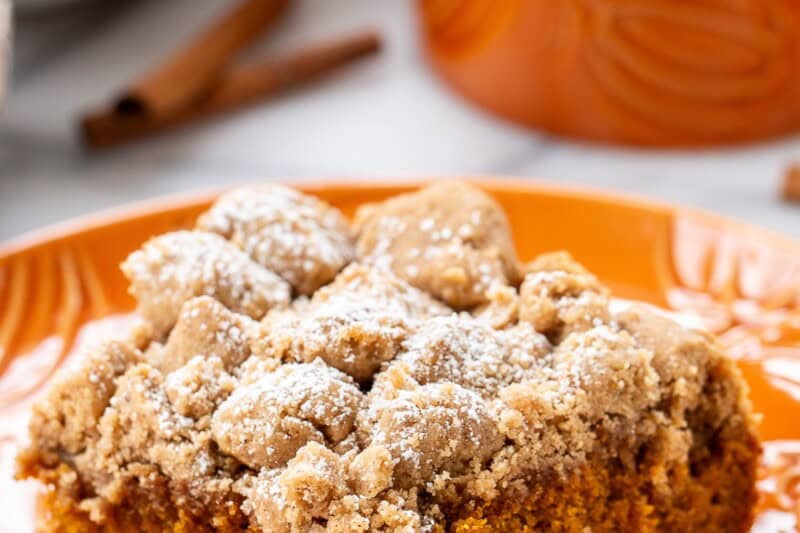 A piece of pumpkin crumb cake on an orange plate with a fork.