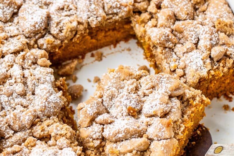 An overhead photo of a sliced pumpkin crumb cake with a spatula lifting one piece.